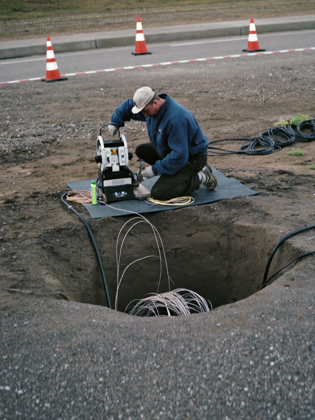 Crew guiding conduit at a directional bore pit on a roadside right-of-way