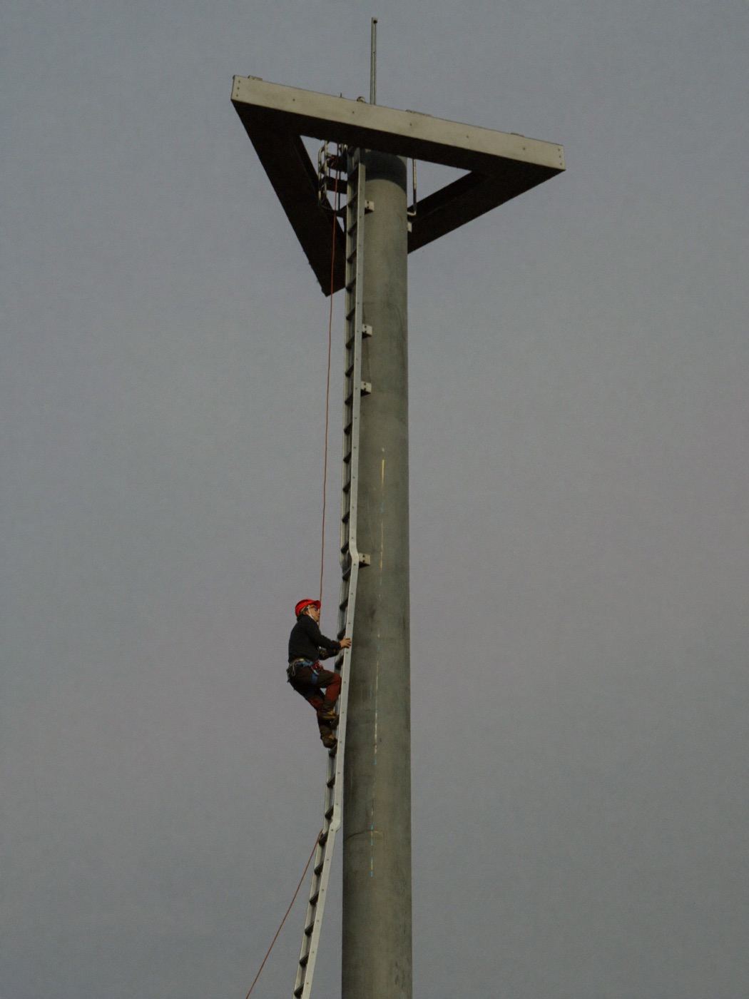 Tower technicians in climbing harnesses rigging an antenna panel at height on a steel monopole